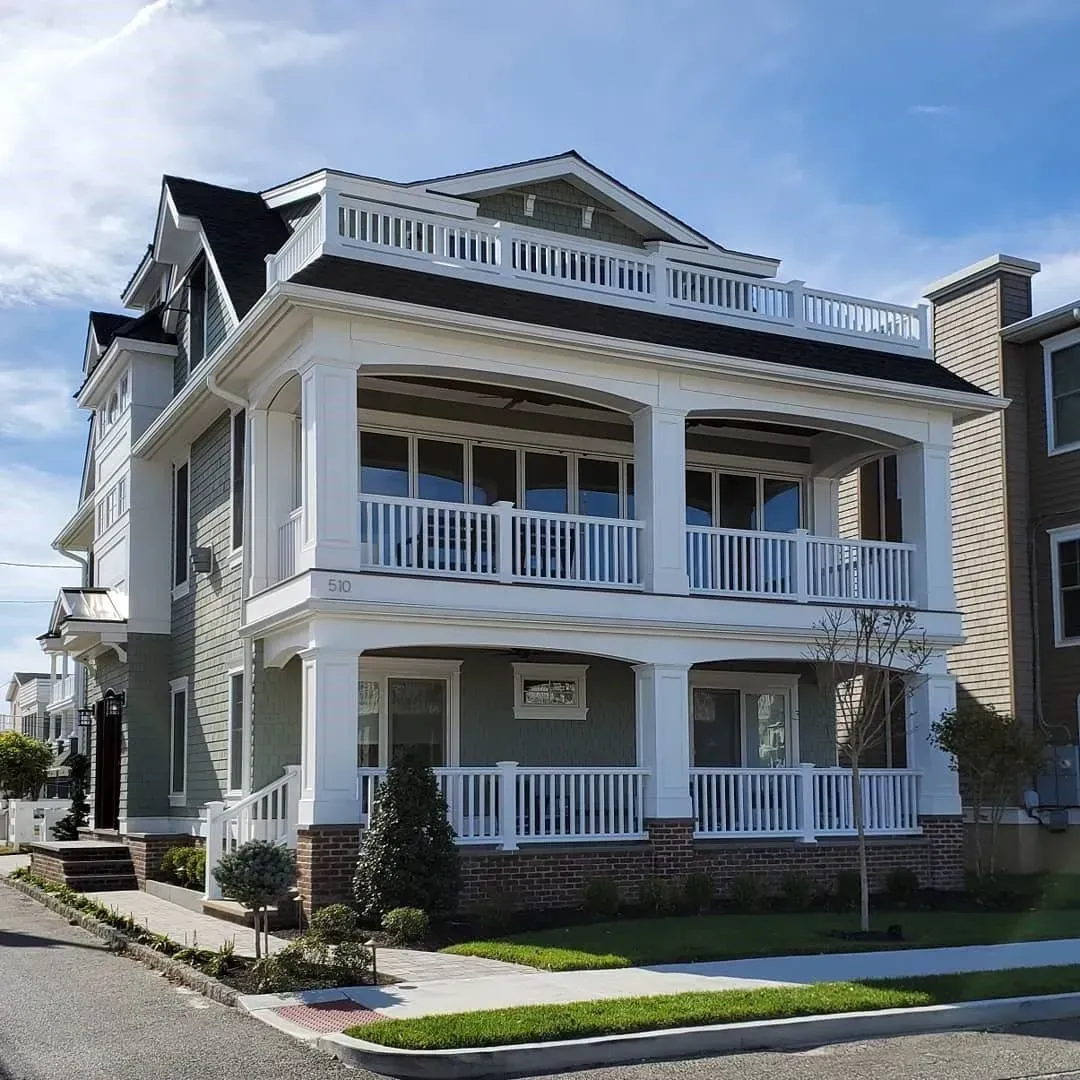 Three-story house with white balconies, green siding, and a rooftop deck under a blue sky.