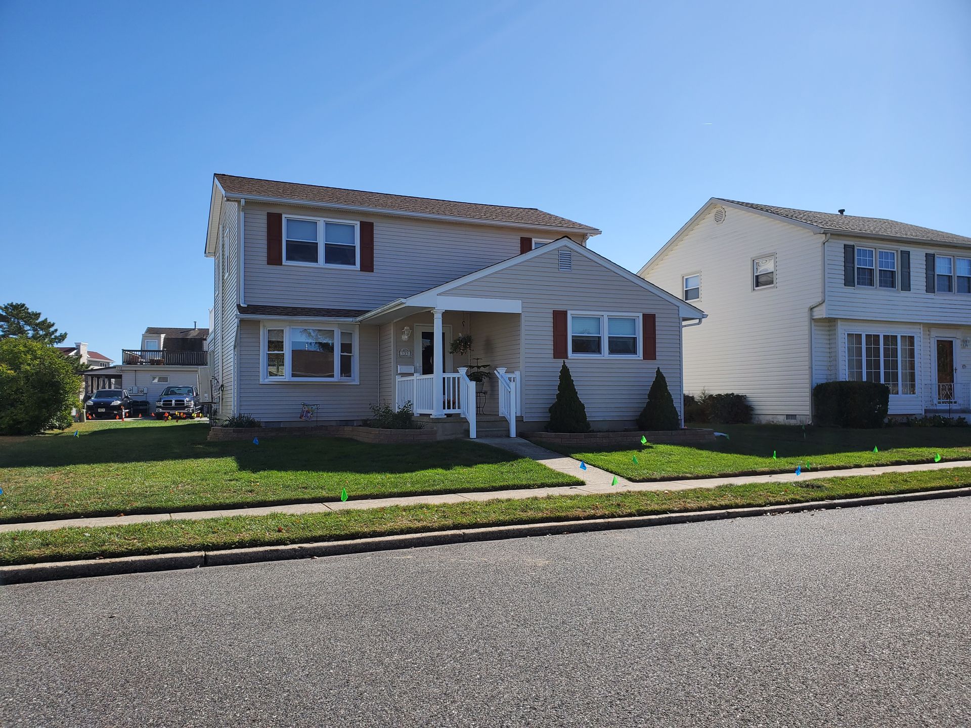Two-story beige house with red shutters and white porch, on a sunny day.