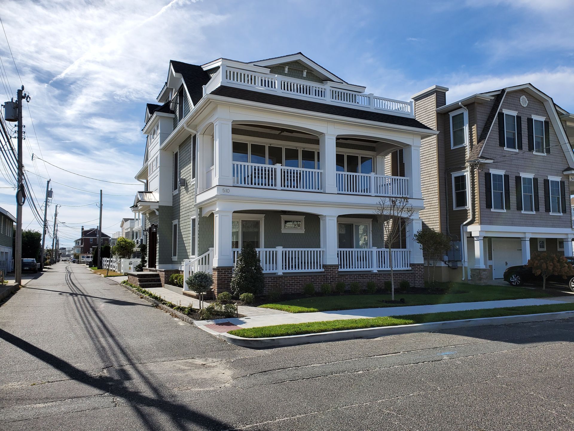 Two-story house with white trim, porch, and a sidewalk; street with telephone poles in front of it.