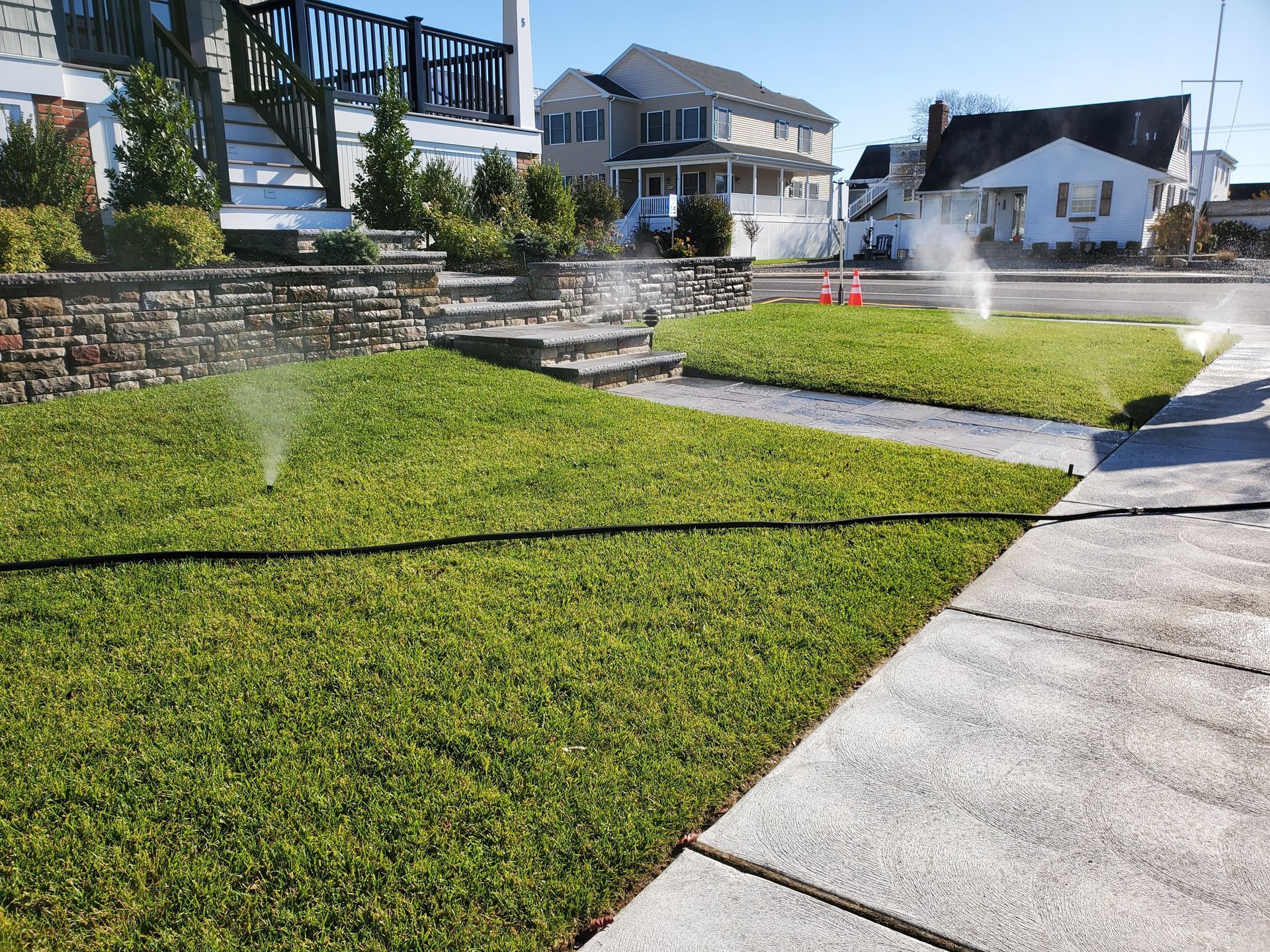 Sprinklers watering green lawns in front of houses on a sunny day.