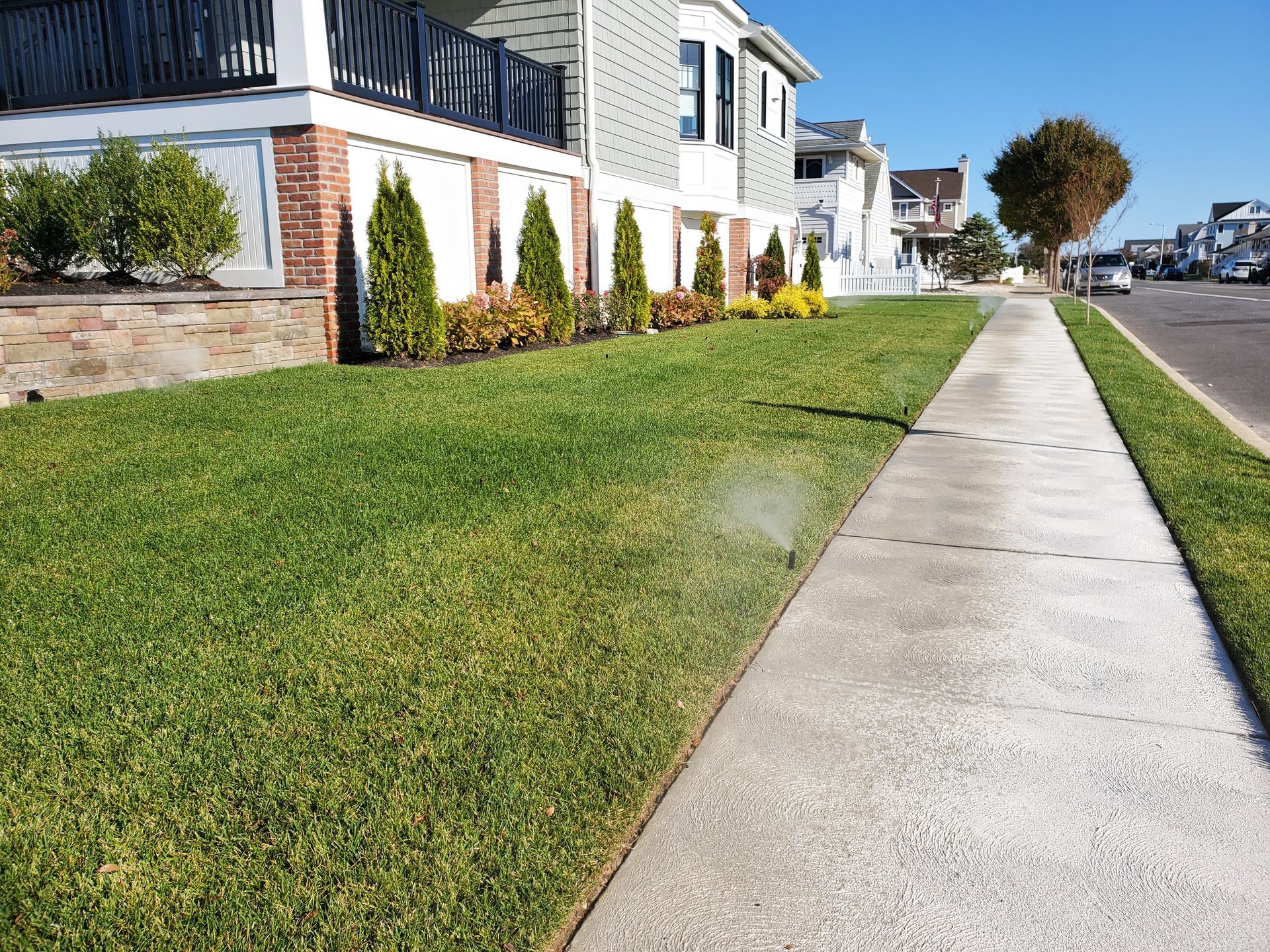 Lush green lawn with sidewalk beside a street, lined with houses, sunny day.