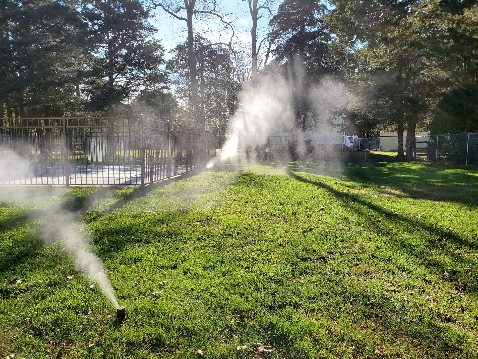 Sprinklers spraying water onto a green, grassy hill in a park, with trees in the background.