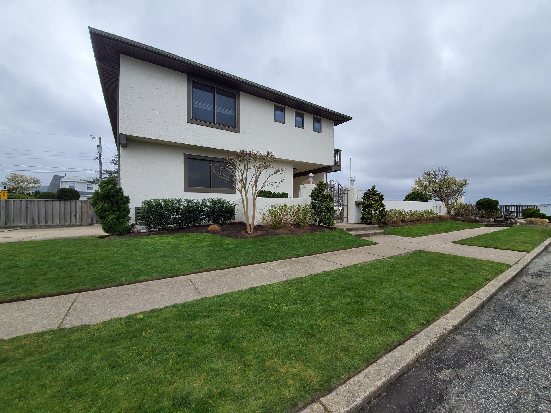 Two-story white house with brown trim and lawn in front, cloudy sky.