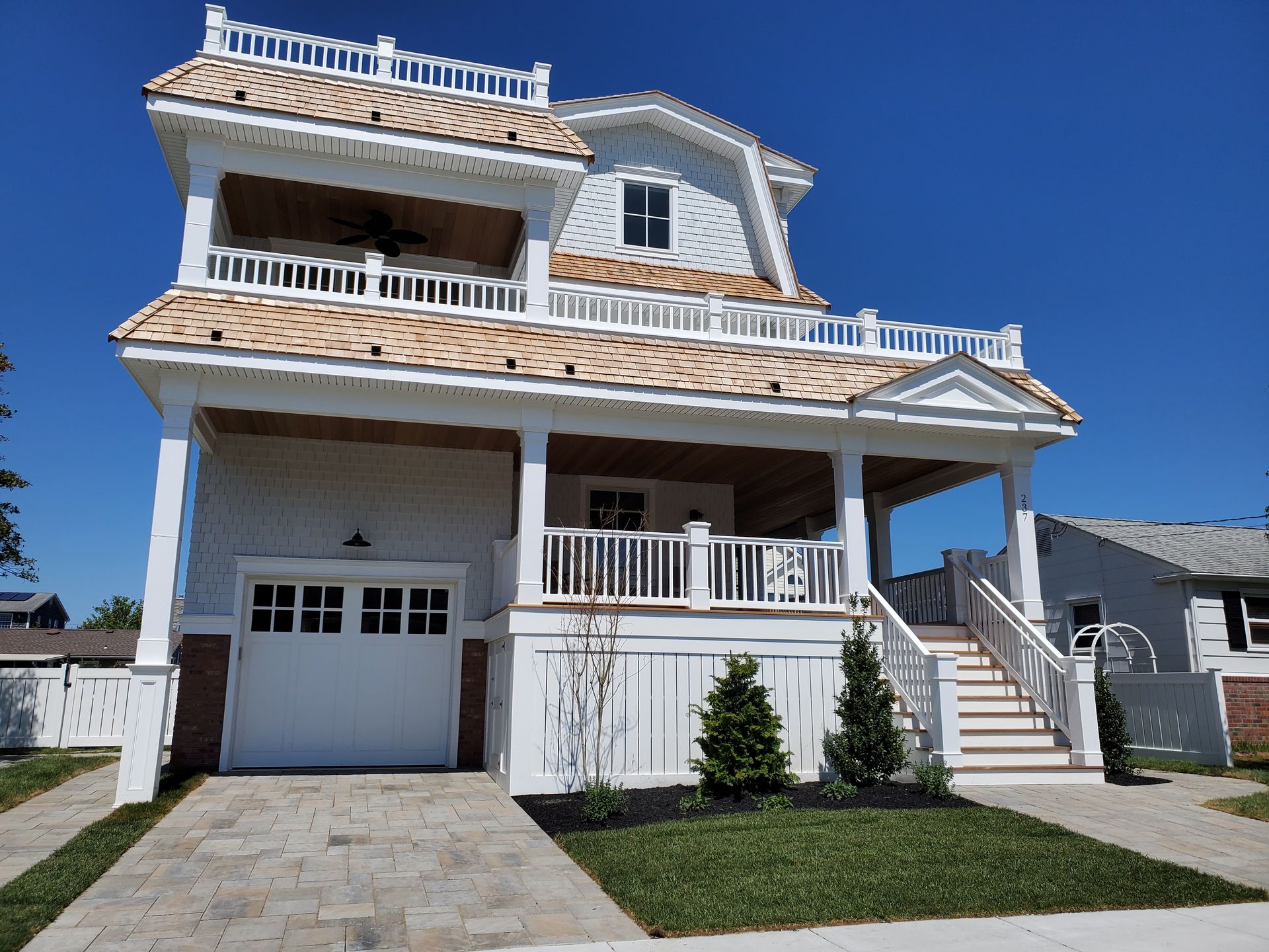 White beach house with tan roof, front porch, and garage, under a blue sky.