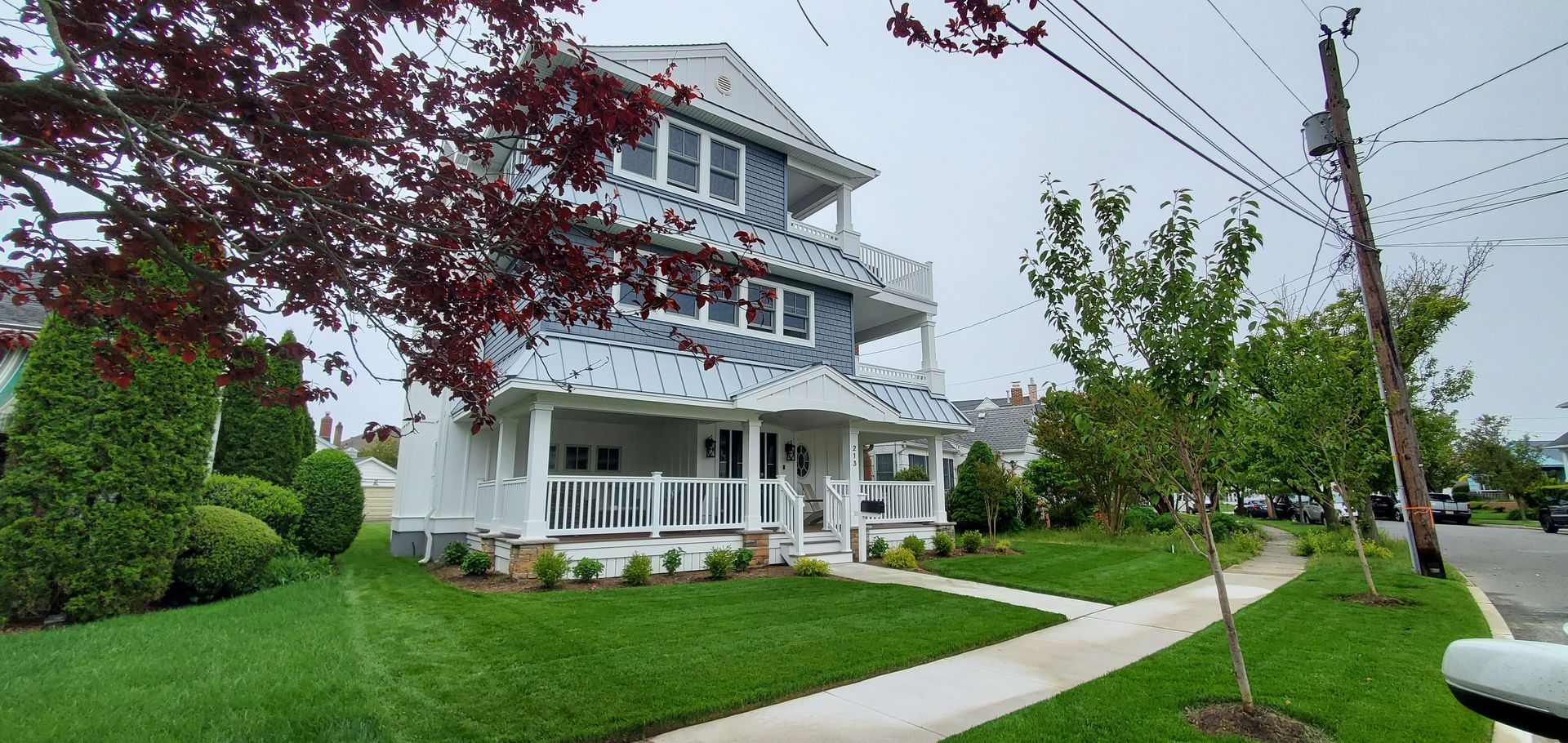 Three-story white house with blue siding, two balconies, and a porch, on a green lawn with trees.