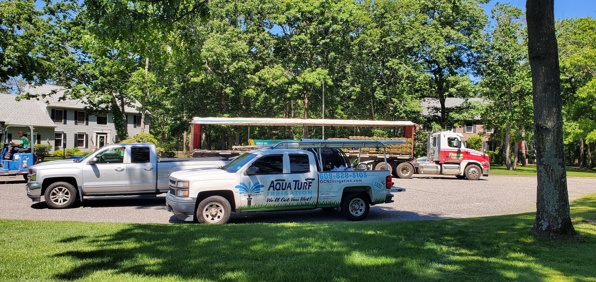 Several trucks parked on a gravel area, with trees and a building in the background.