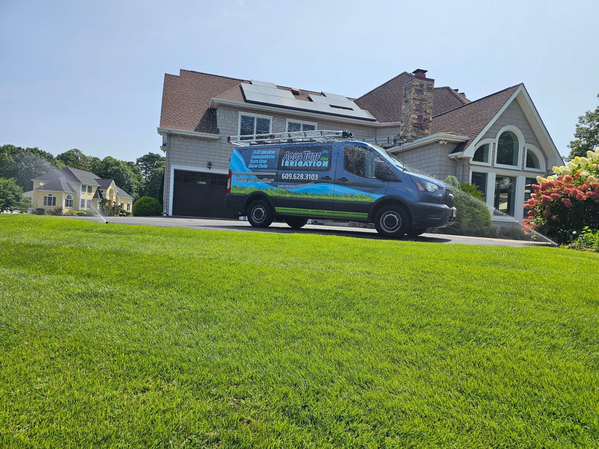 A blue service van parked in front of a house on a sunny day with green grass in the foreground.