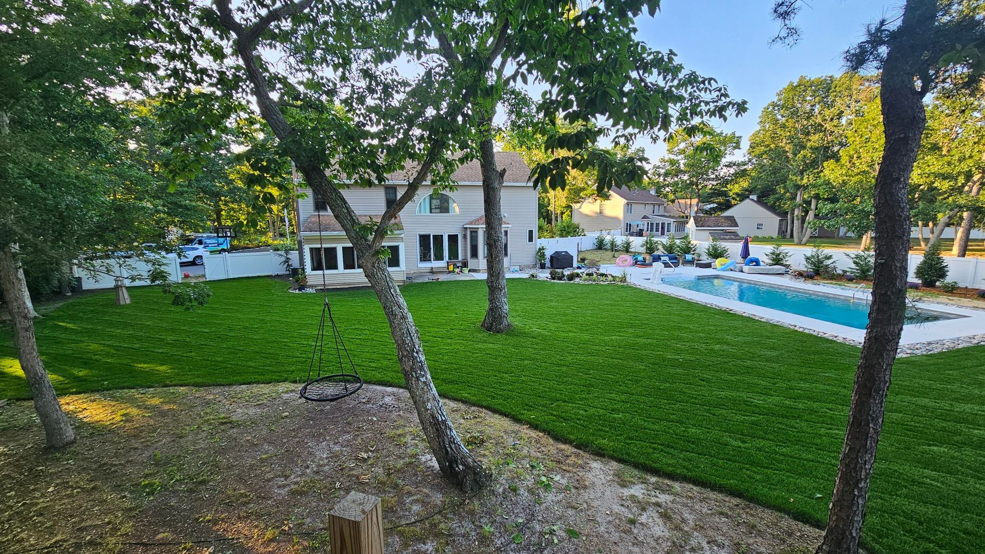 A large house with a pool and lawn surrounded by trees, viewed from an elevated perspective.