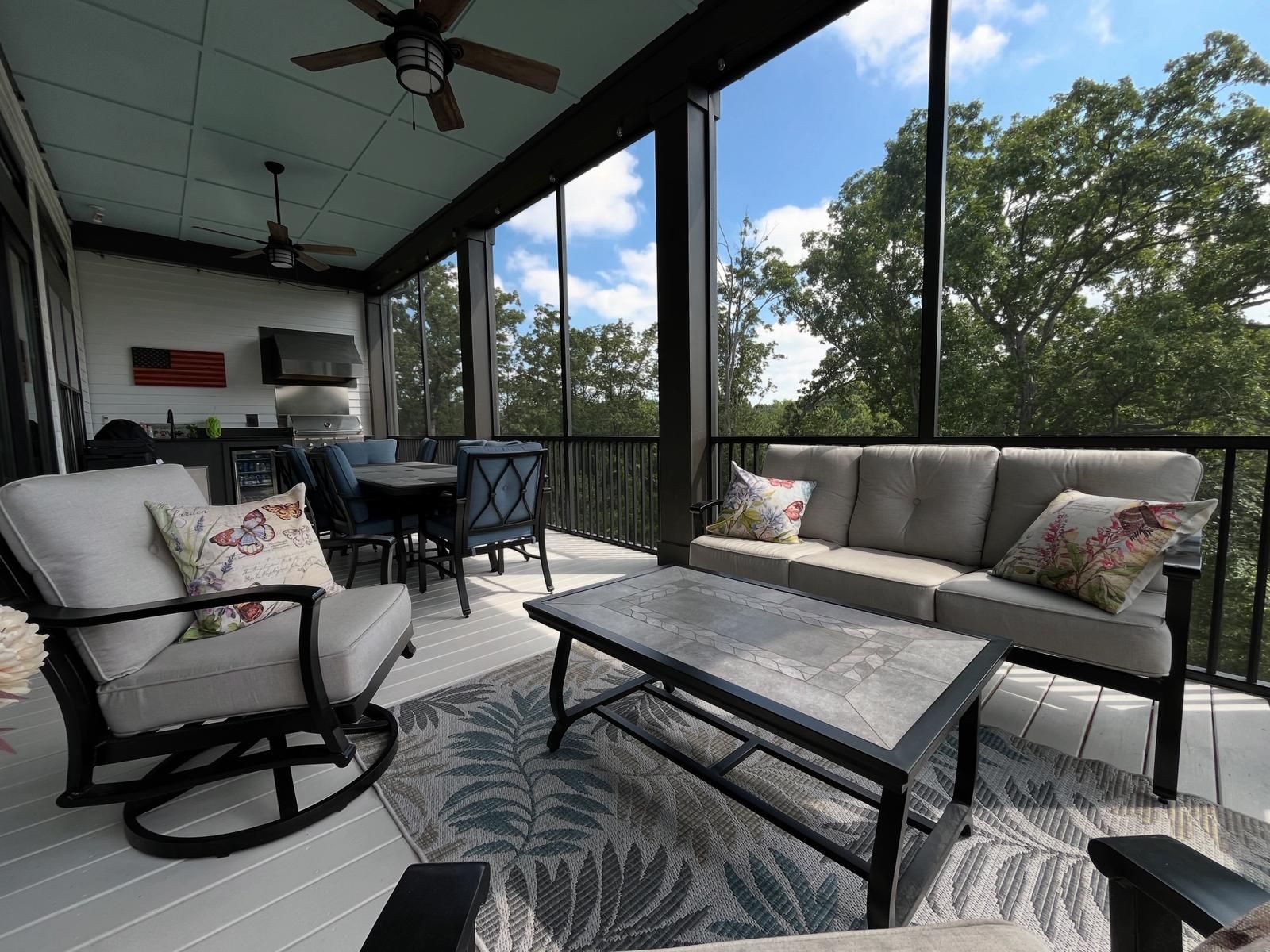 Screened porch with gray furniture, a rug, and a view of trees.
