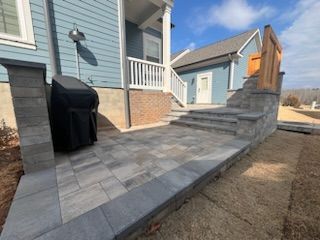 Blue house with stone patio and steps leading to a porch, a grill, and a wooden fence.