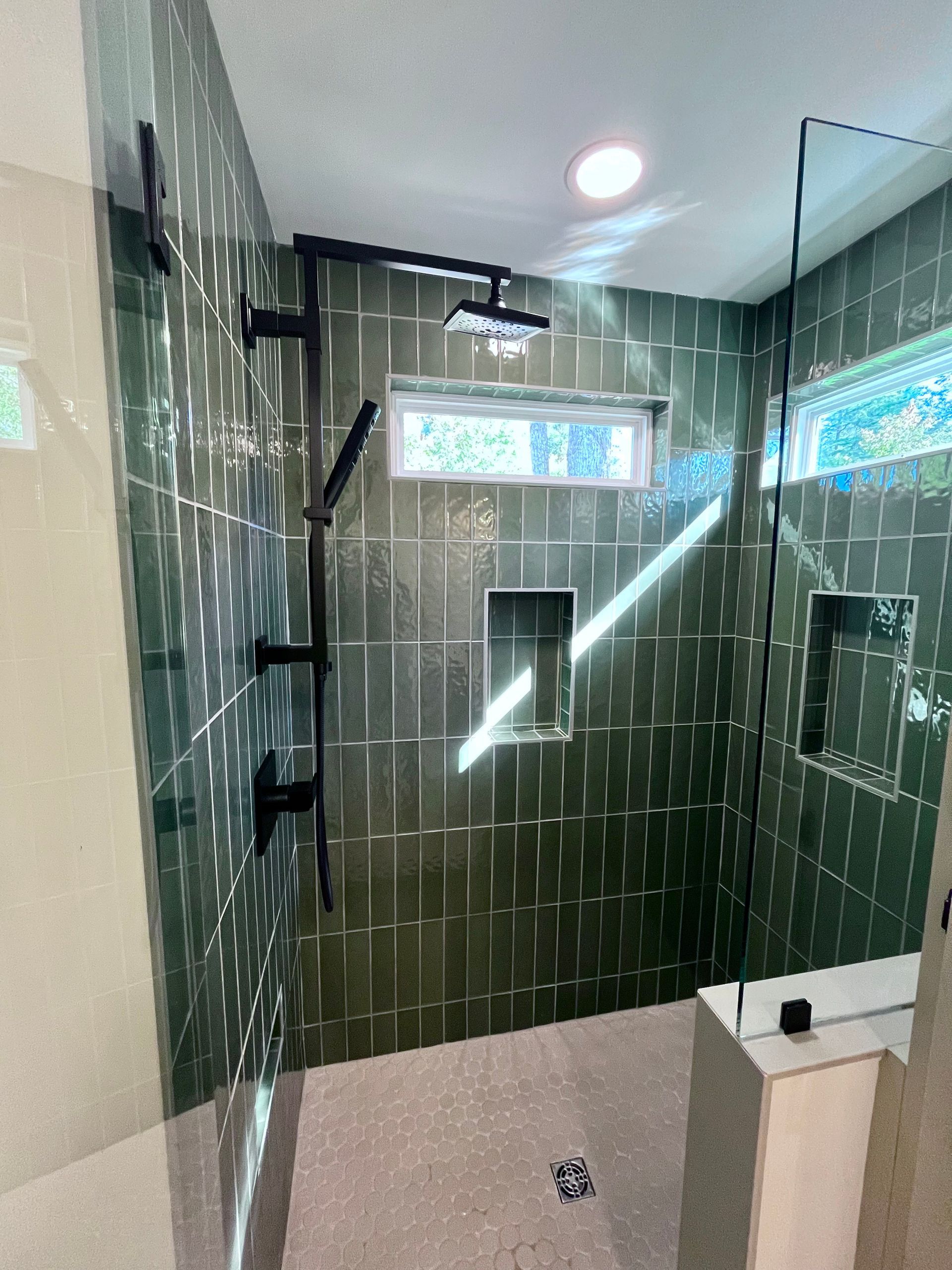 Green tiled shower with black fixtures, a window, and glass enclosure.