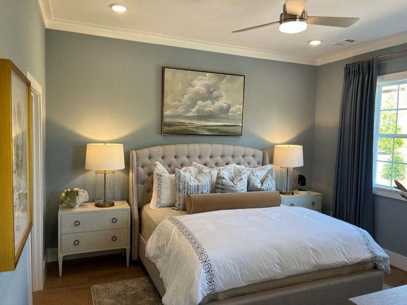 Bedroom with a tufted headboard, two nightstands, and an artwork above the bed. Soft blue walls and white bedding.