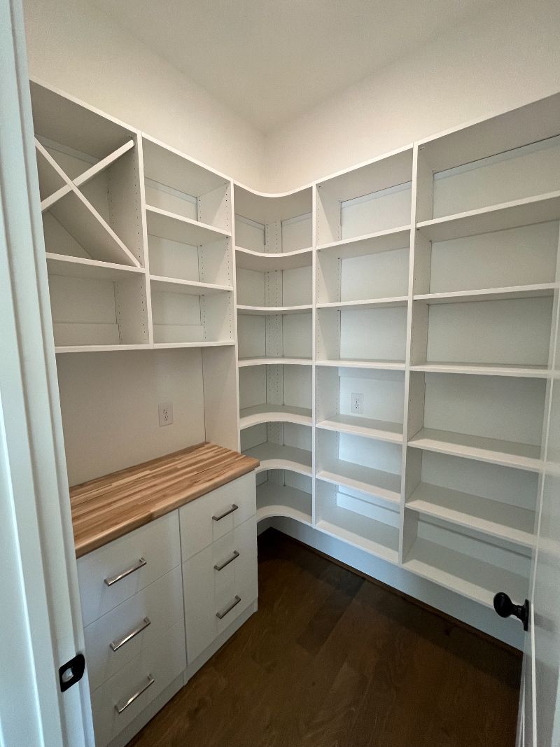 White pantry with shelves, wine rack, cabinets, and butcher block counter.