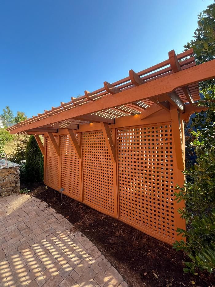 Wooden trellis and pergola in a garden setting, painted orange against a blue sky.