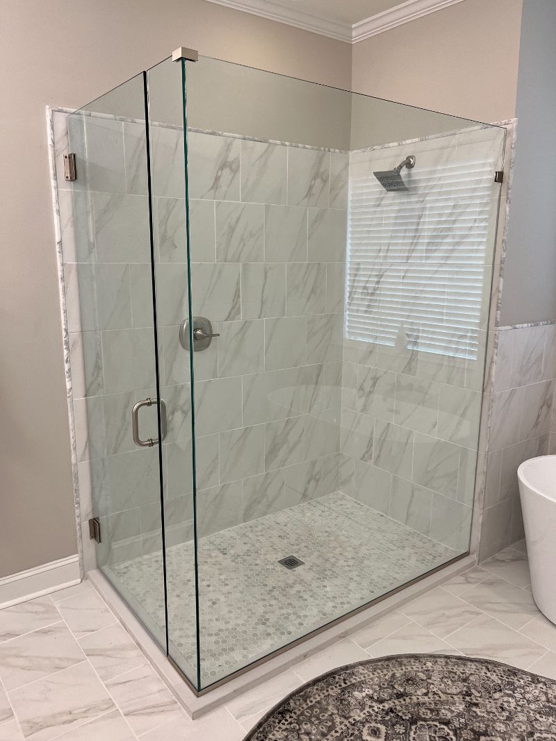 Glass shower enclosure with tiled walls, silver shower fixtures, and small stone floor.