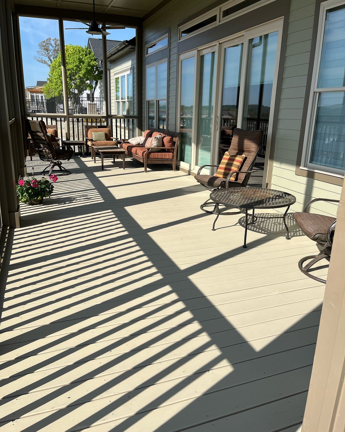 A screened porch with outdoor furniture, casting striped shadows on a sunny day.