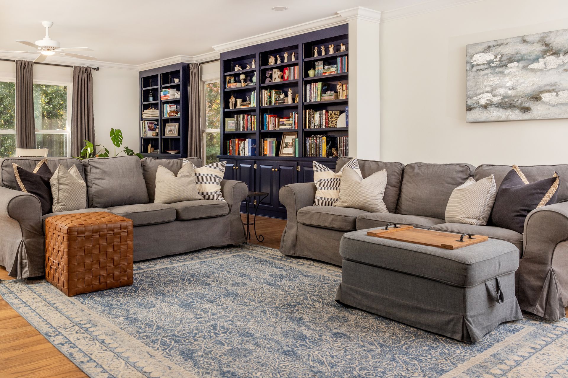 Living room with blue bookcase, gray sofas, blue patterned rug, and brown ottoman.