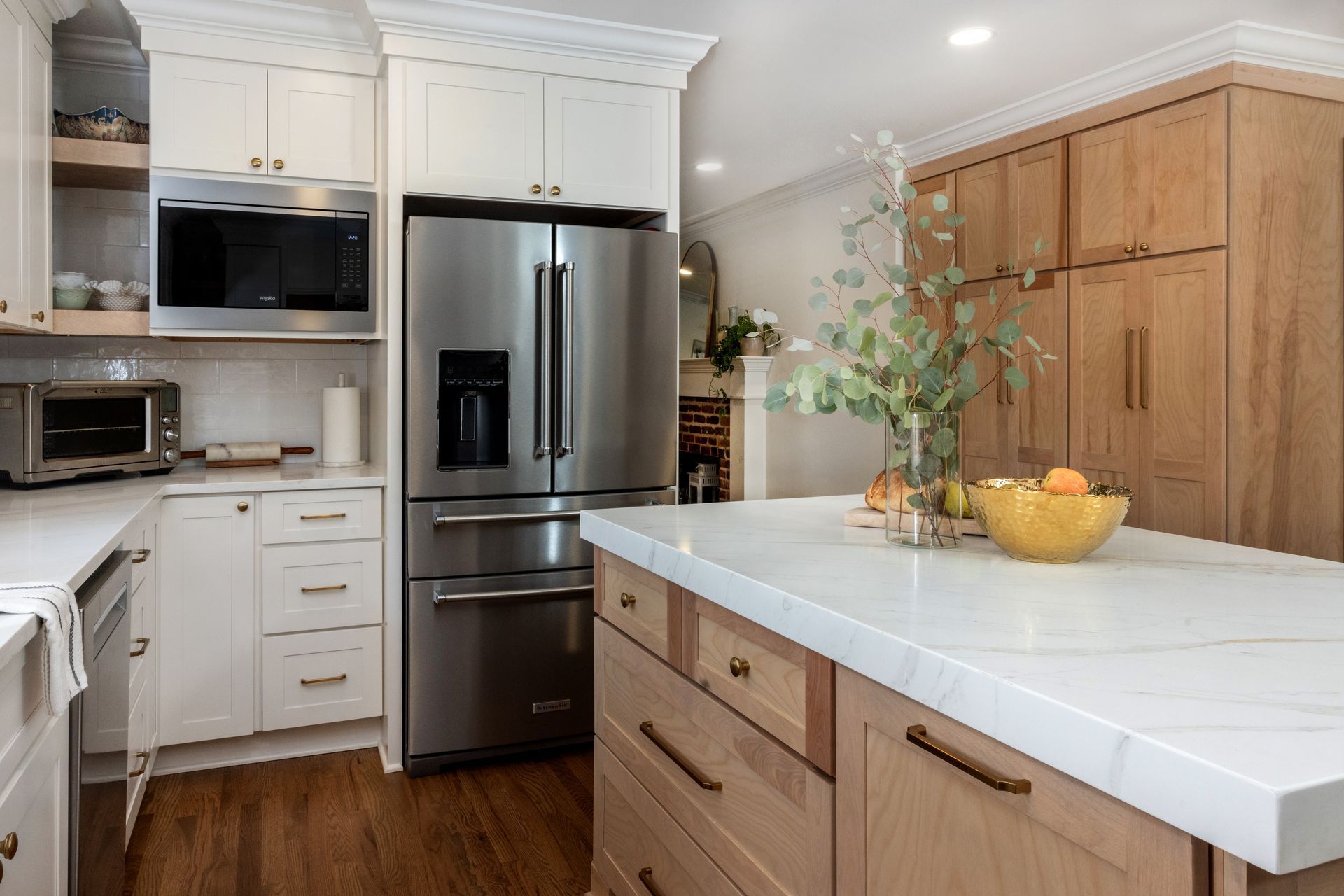 Modern kitchen with white and wood cabinets, stainless steel refrigerator, and island with quartz countertop.