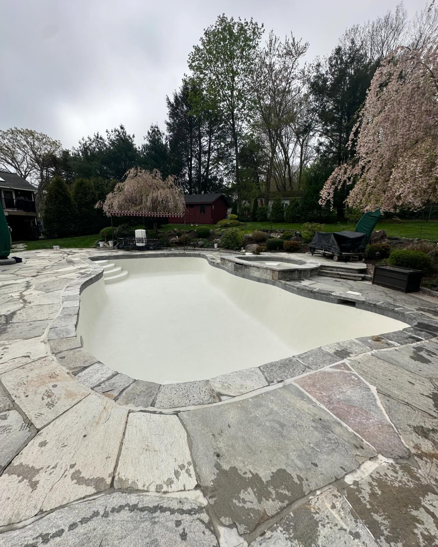 A large white swimming pool surrounded by stone and trees