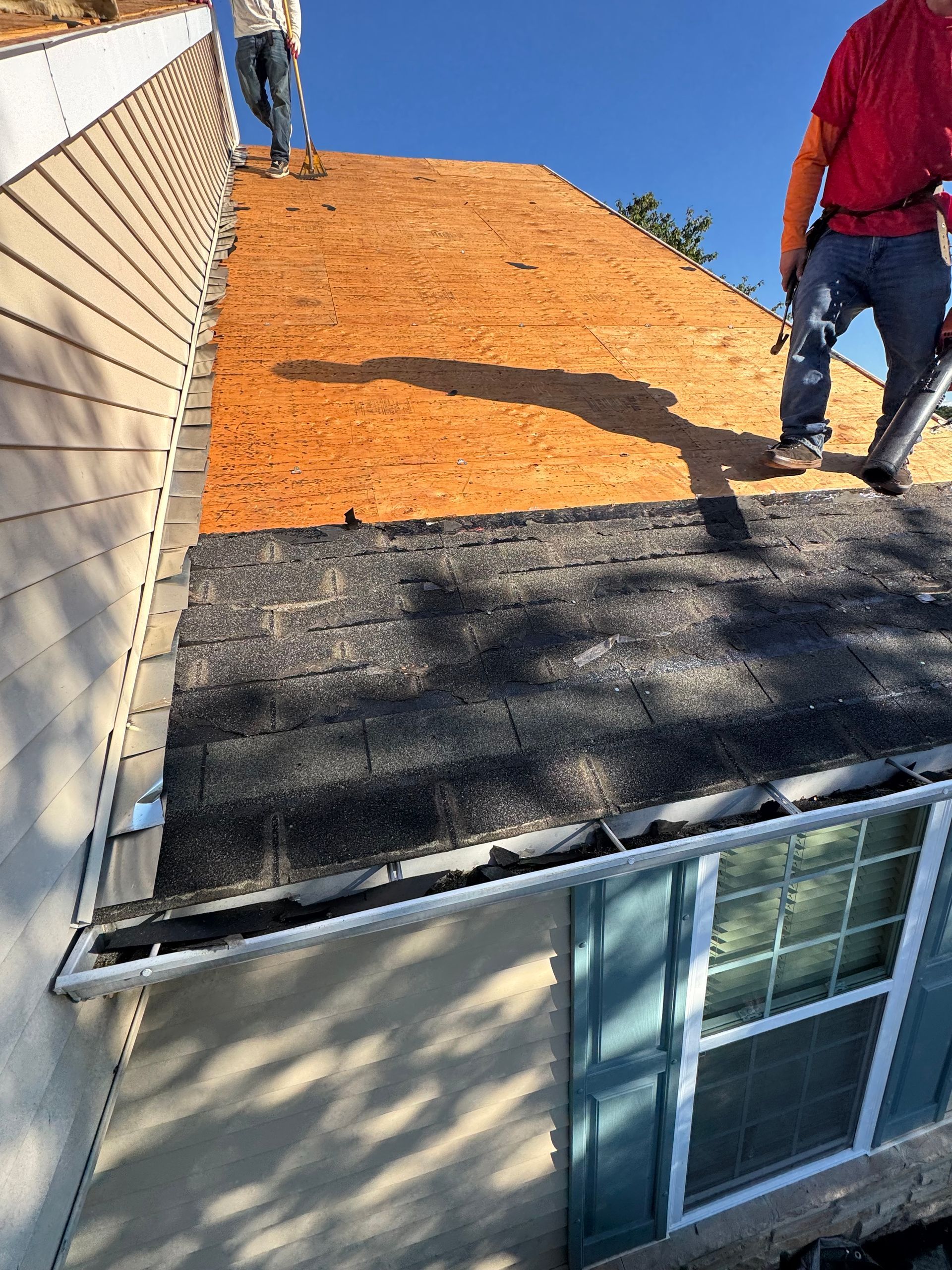 Workers replacing a roof, partially completed. One section has new black shingles, the rest is exposed underlayment.