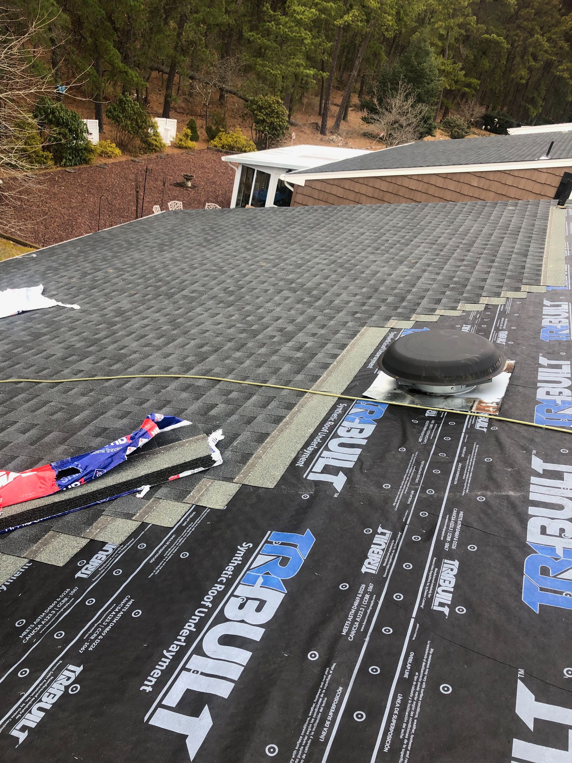 Roof with shingles being installed; a ventilation pipe and roofing materials are visible.