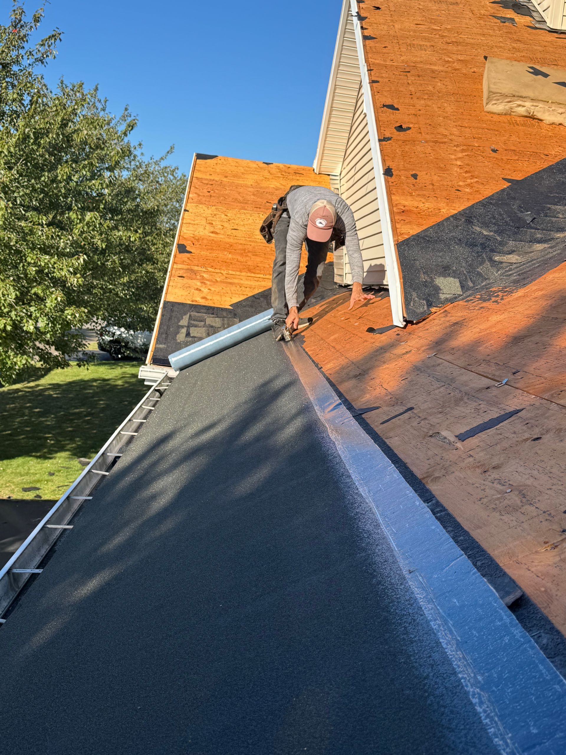 Roofer installing flashing on a roof, applying sealant, wearing a cap and working in the sunshine.