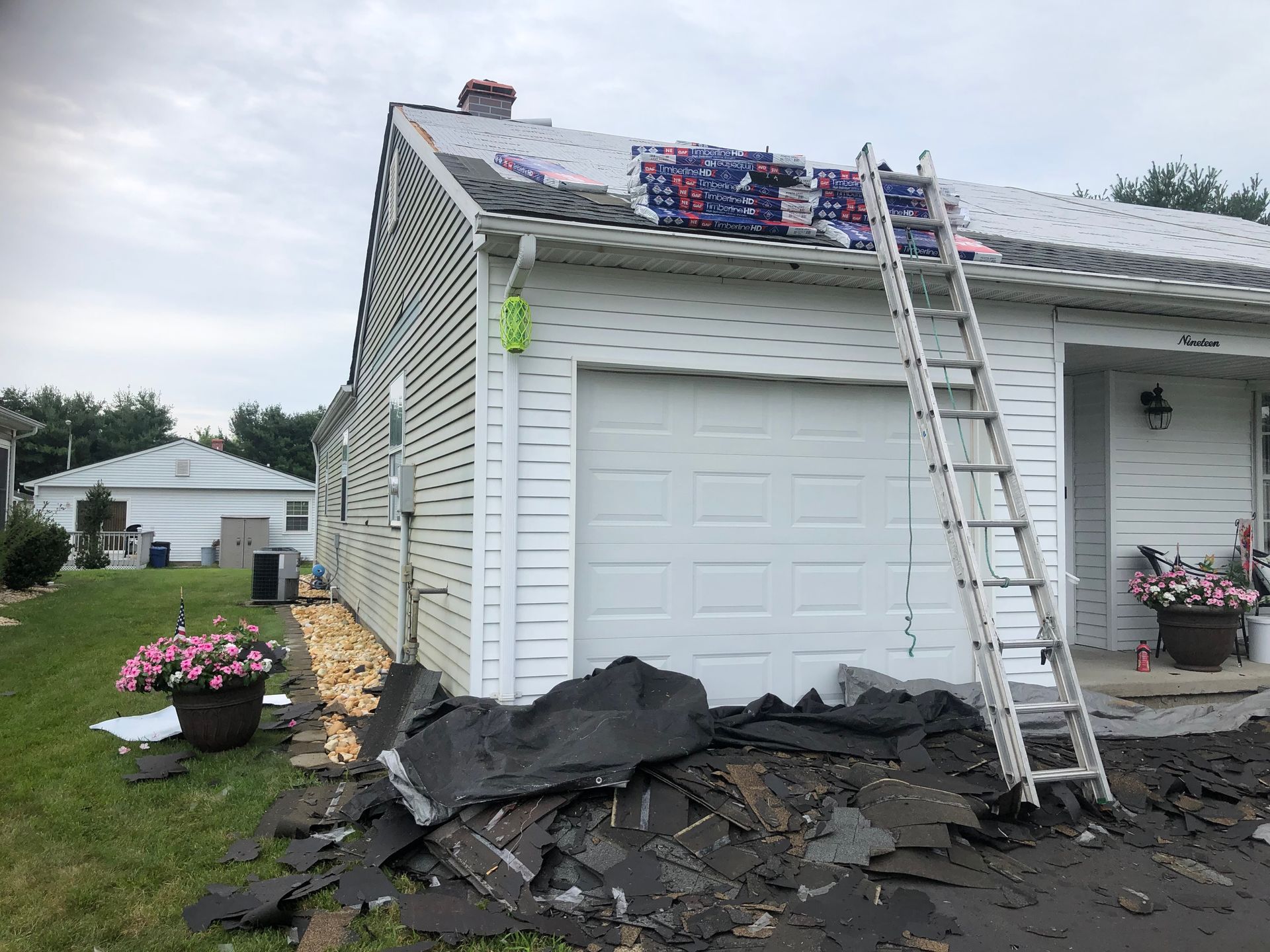 Roof partially under construction on a white house; ladder, shingles, and debris visible.