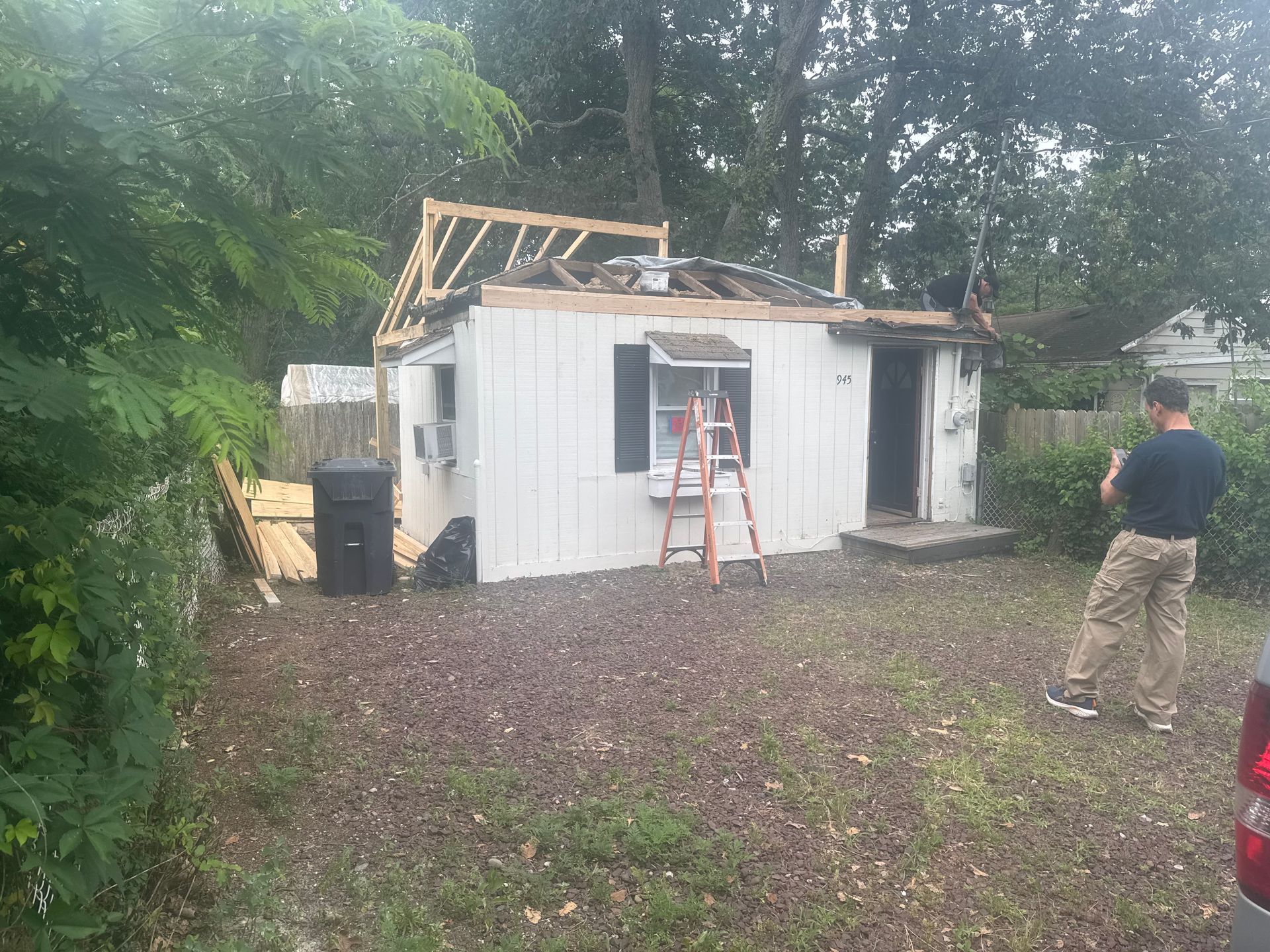 A white shed with a partially removed roof is being worked on. A person stands nearby.