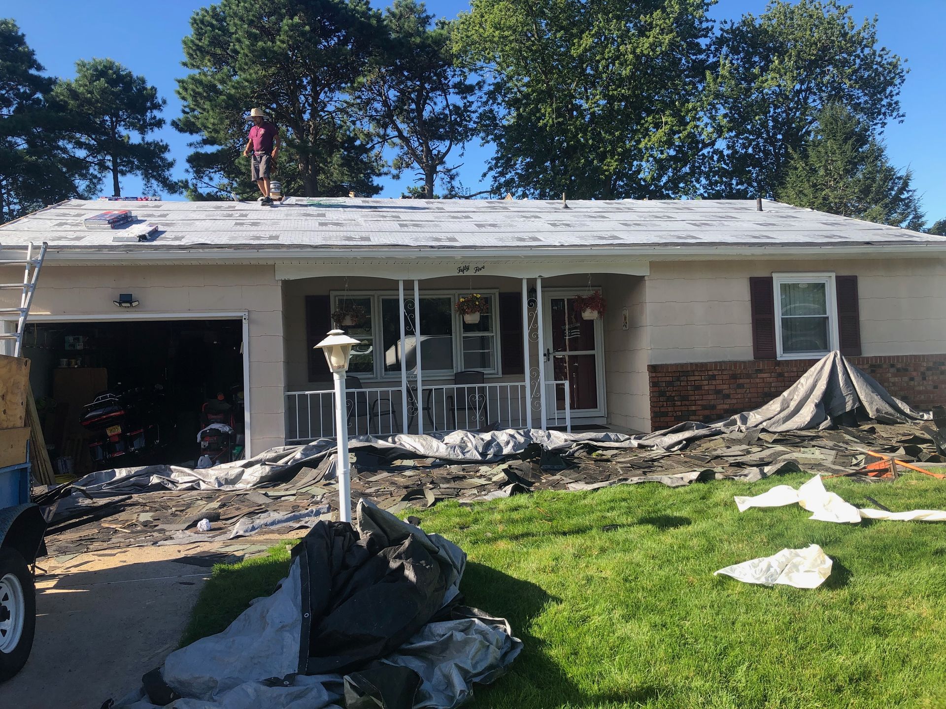 Home with roof replacement in progress; debris on the ground. A worker stands on the roof.