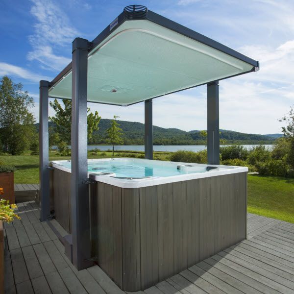 A hot tub with a canopy over it sits on a deck overlooking a lake