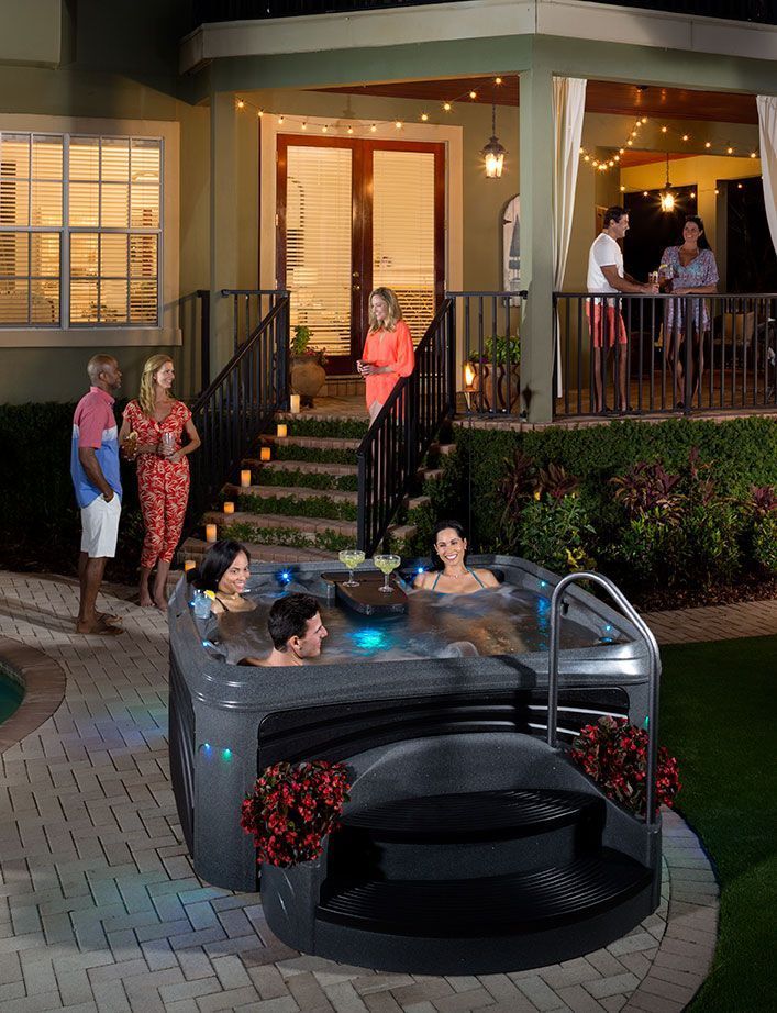 A group of people are sitting in a hot tub outside of a house