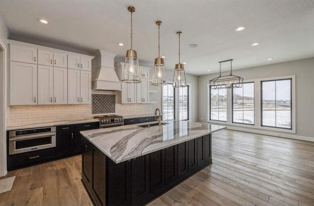 Modern kitchen with white cabinets, dark island, stainless appliances, and large windows overlooking a snowy view