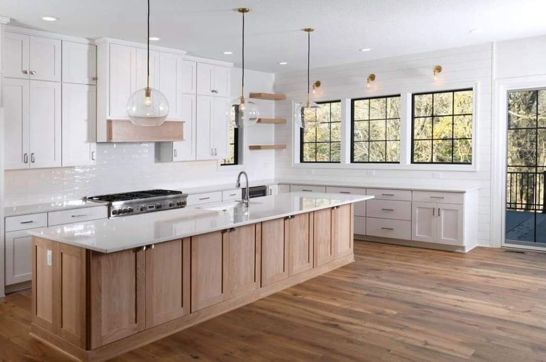 Bright modern kitchen with white cabinets, wood island, and large windows overlooking trees
