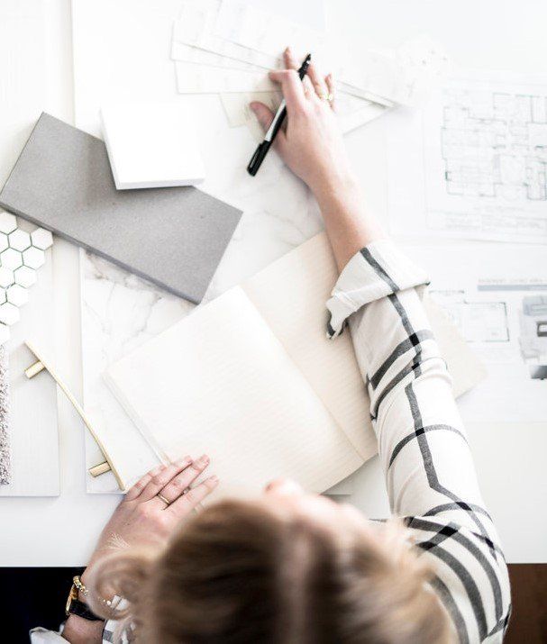 Person sketching a design layout on a desk with paper samples and a pencil