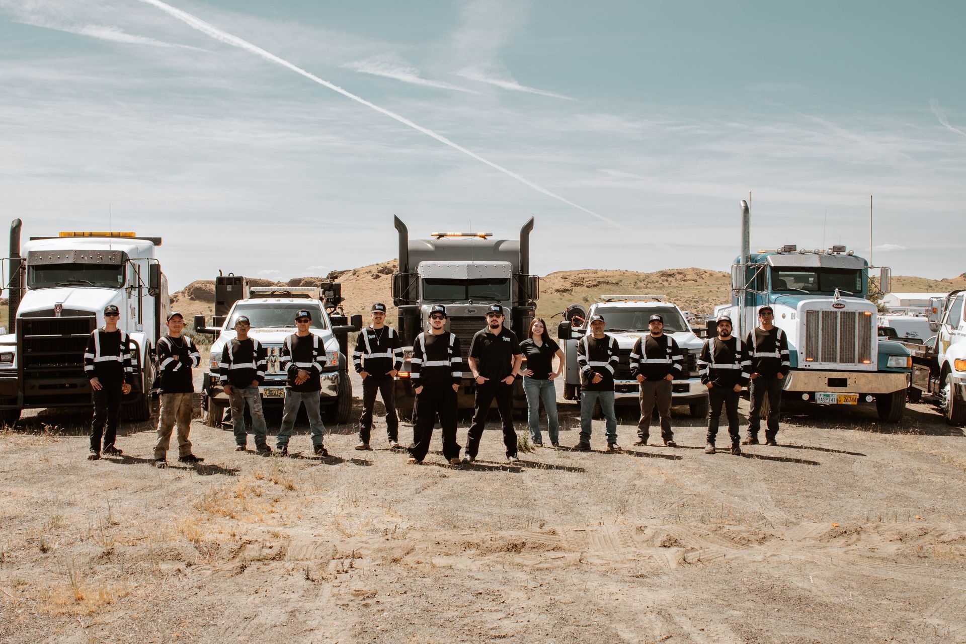 Group of people standing in front of six trucks in a dusty desert landscape under a clear sky