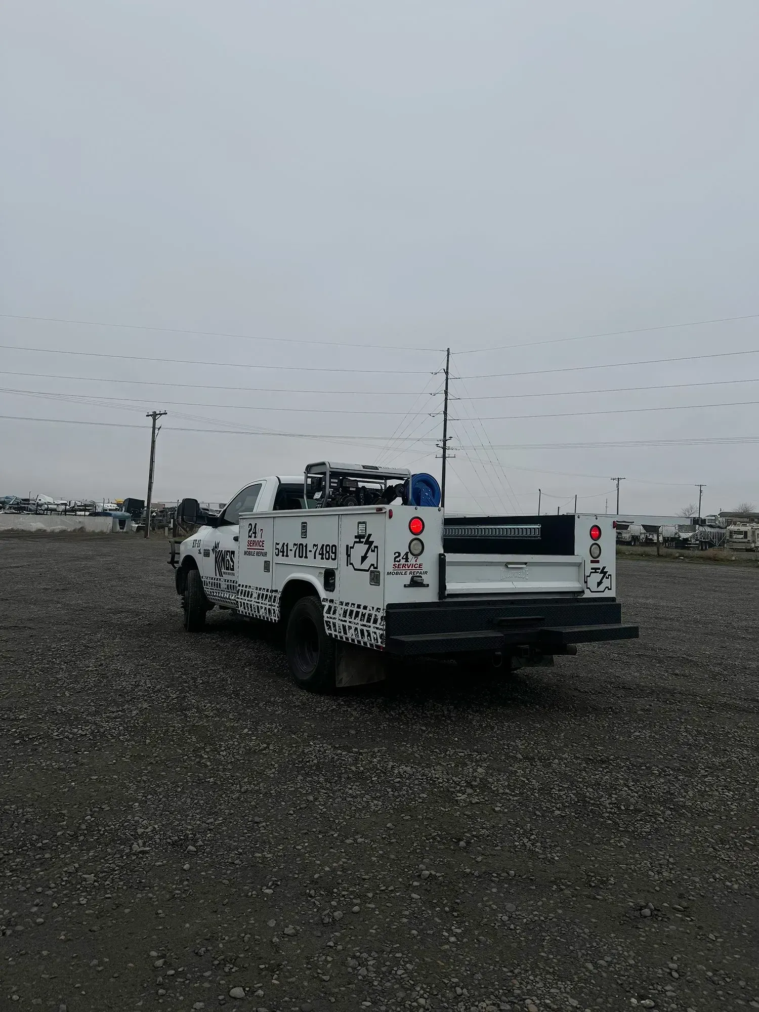 A white work truck with black and white patterned decals parked in a gravel lot under a cloudy sky.