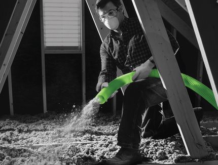 Person kneeling indoors, spraying water from a bright green hose under a wooden structure.