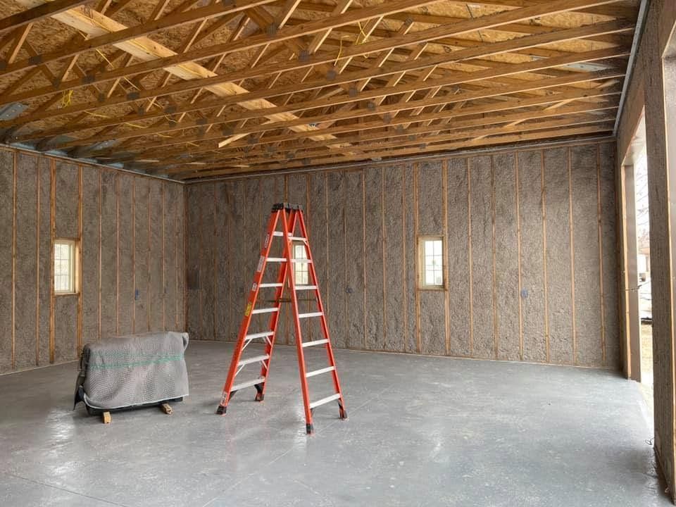 An empty unfinished room with an exposed wood ceiling, a red ladder, and covered equipment on the concrete floor