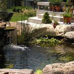 Water pond with a small waterfall, stone steps, and potted plants.
