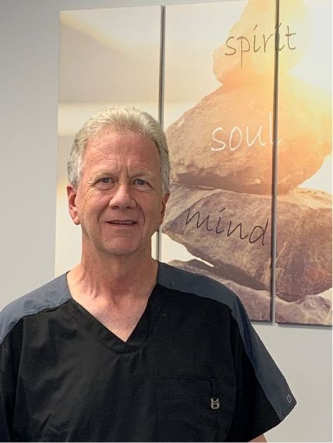 A man in a scrub top is standing in front of a painting of rocks.