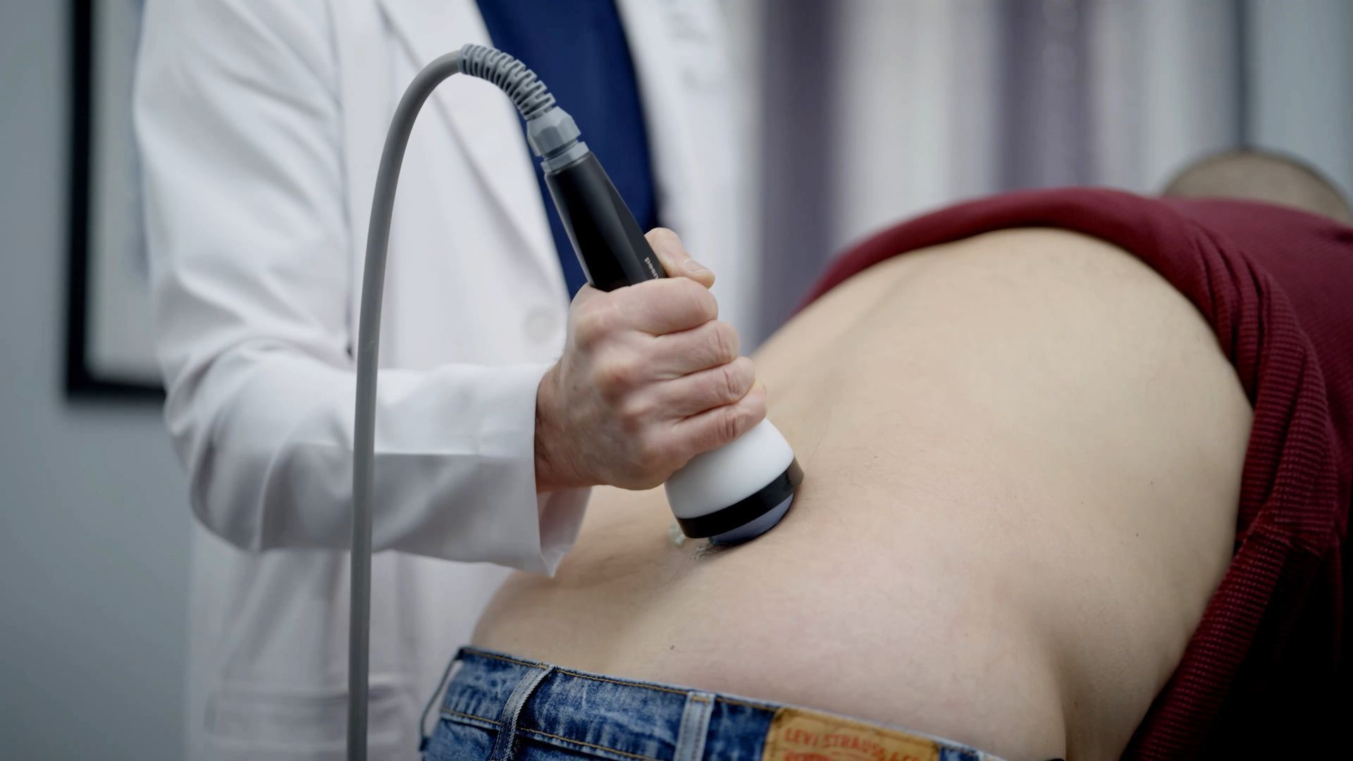 Doctor using a therapy device on a patient's lower back.