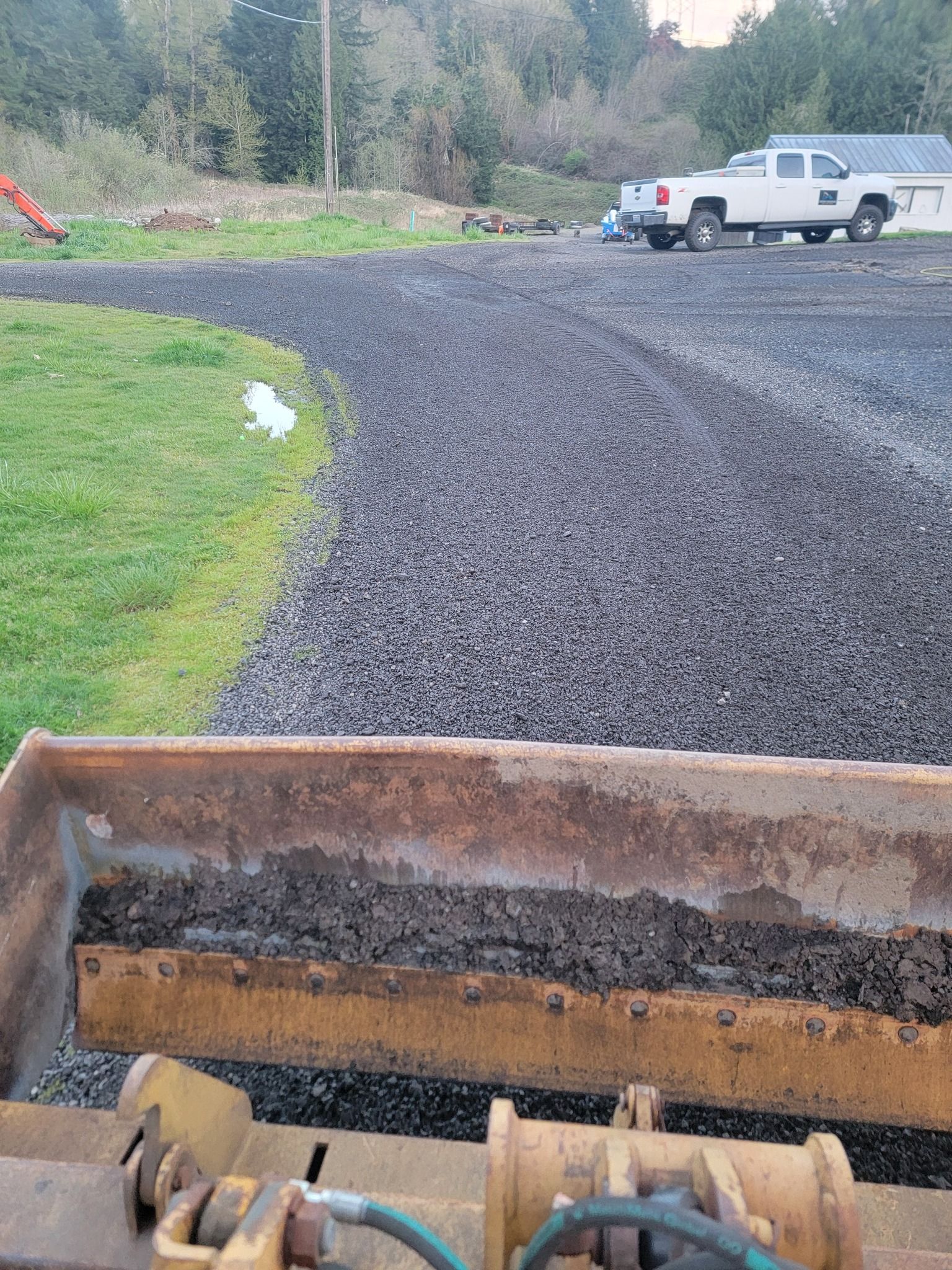 A bucket of dirt is sitting in a parking lot next to a truck.