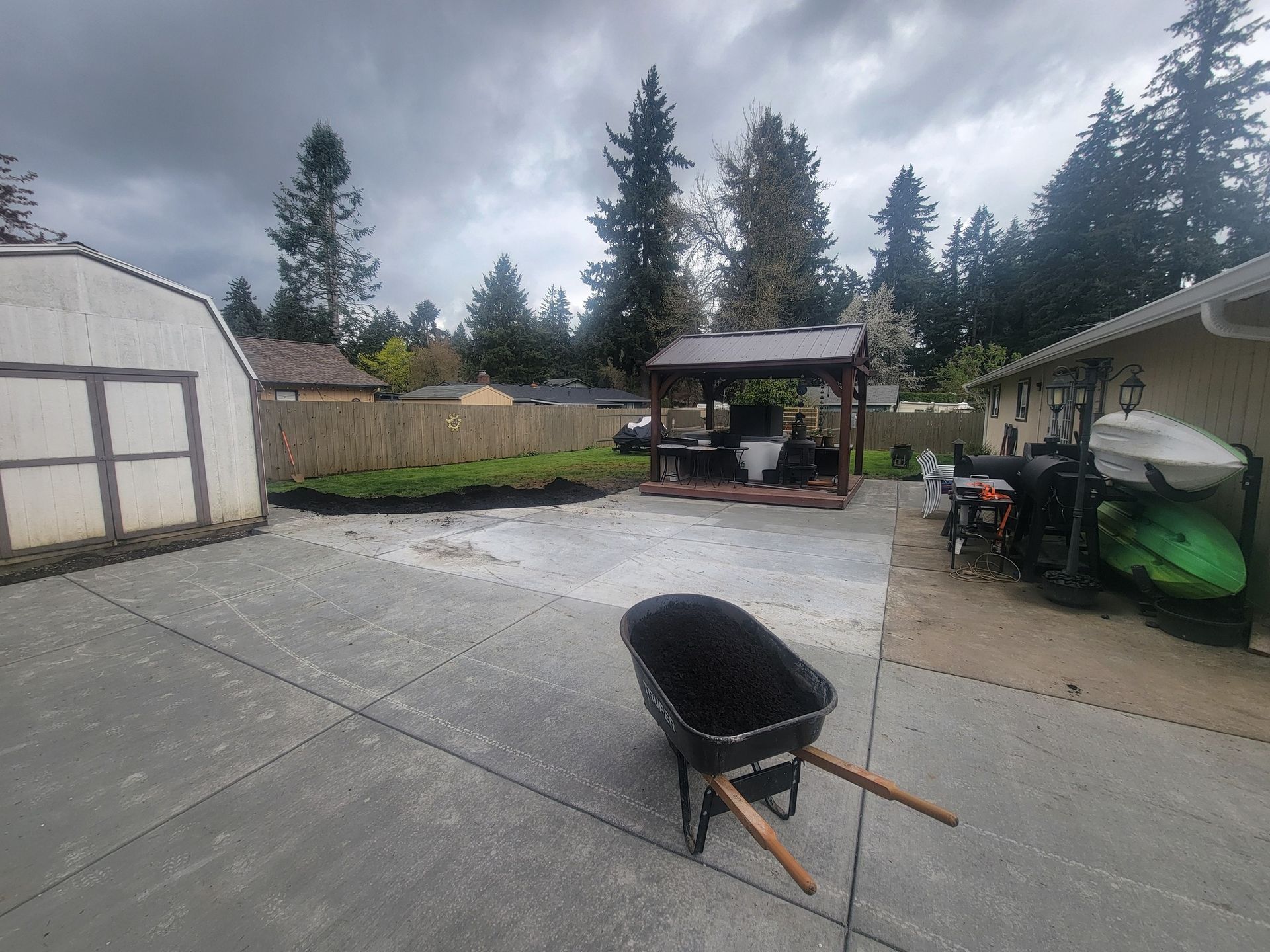 A wheelbarrow is sitting on the sidewalk in a backyard.
