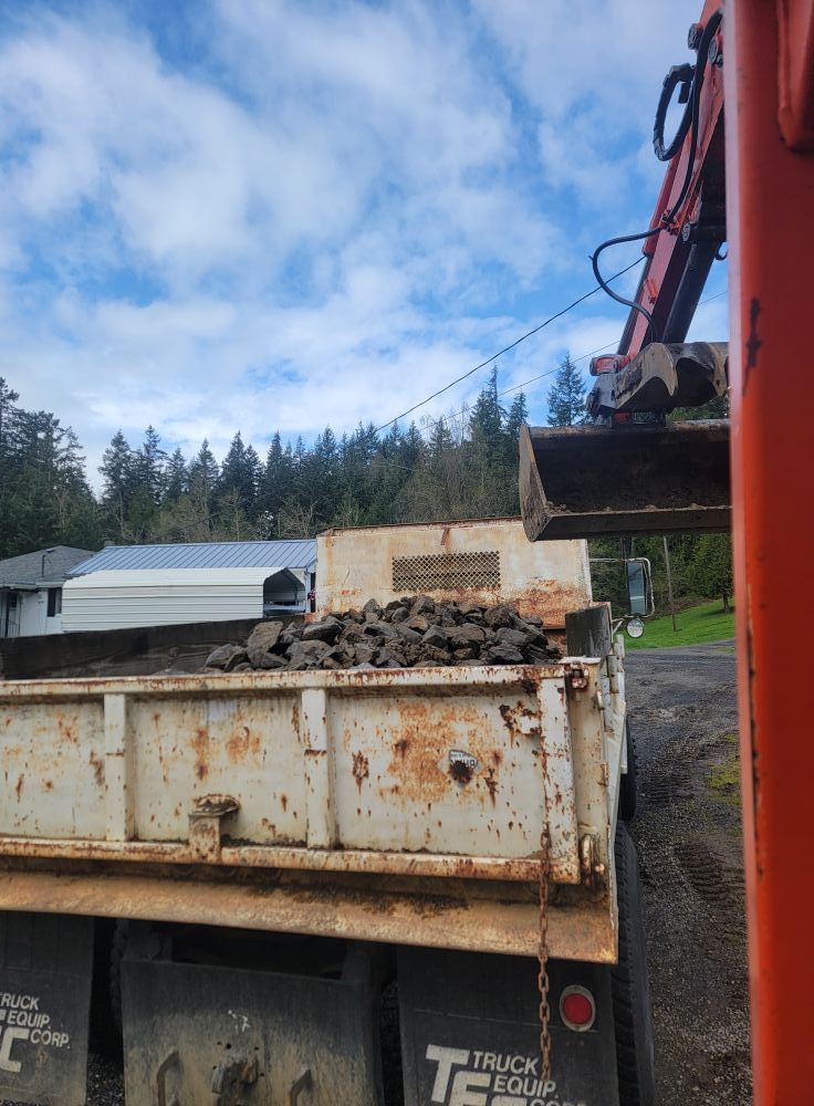 A dump truck is being loaded with rocks by a crane.