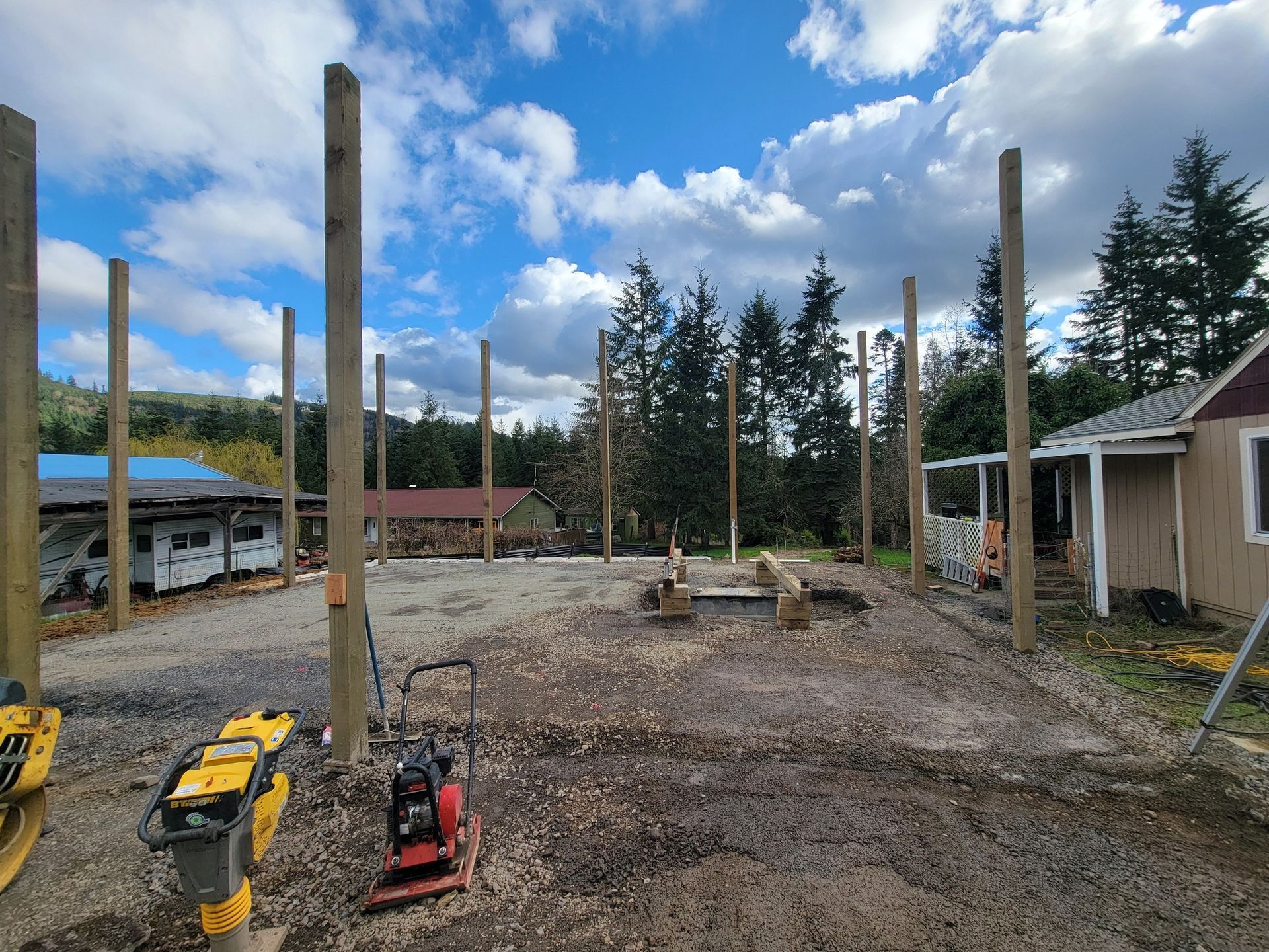 A lot of wooden poles are sitting in the dirt in front of a house.