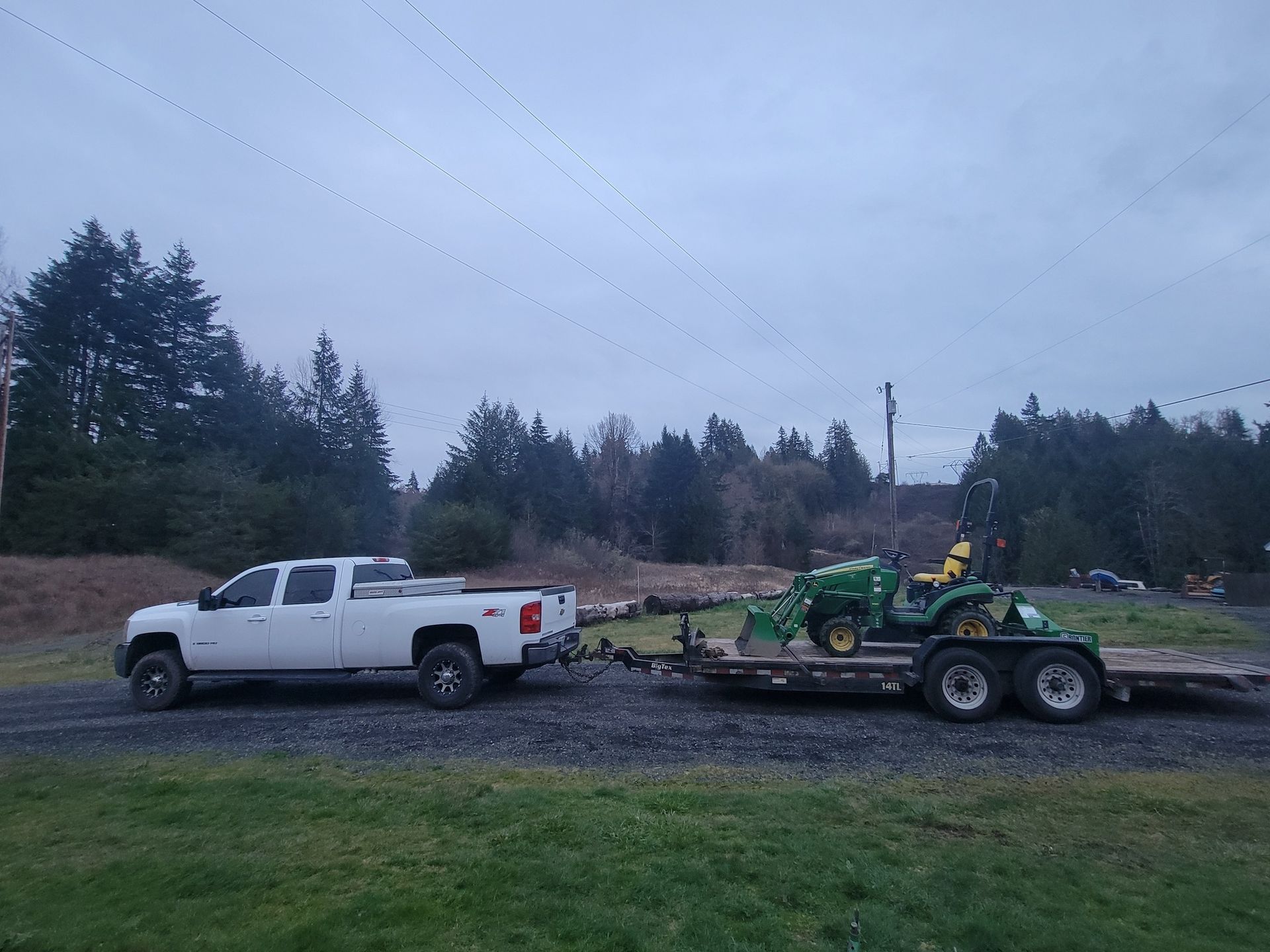 A white truck is towing a green tractor on a trailer.