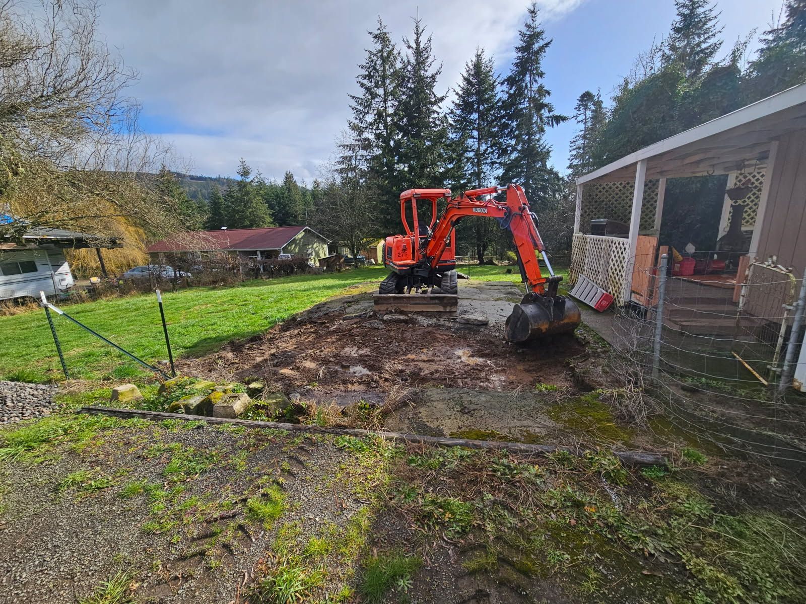 An excavator is digging a hole in a yard in front of a house.