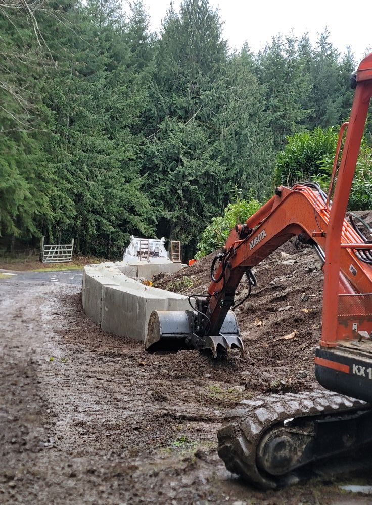 An orange excavator is working on a dirt road in the woods.