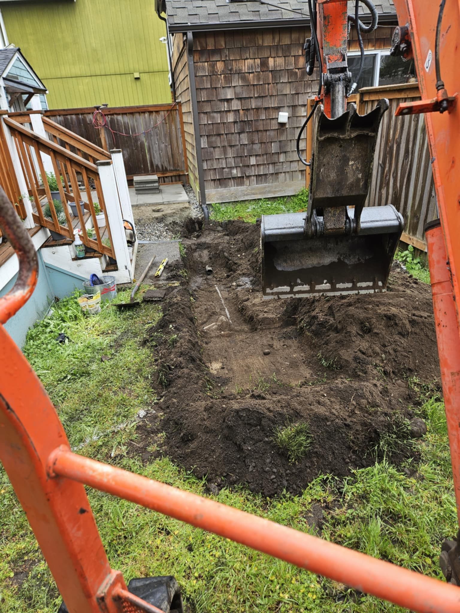 An excavator is digging a hole in the dirt in a backyard.