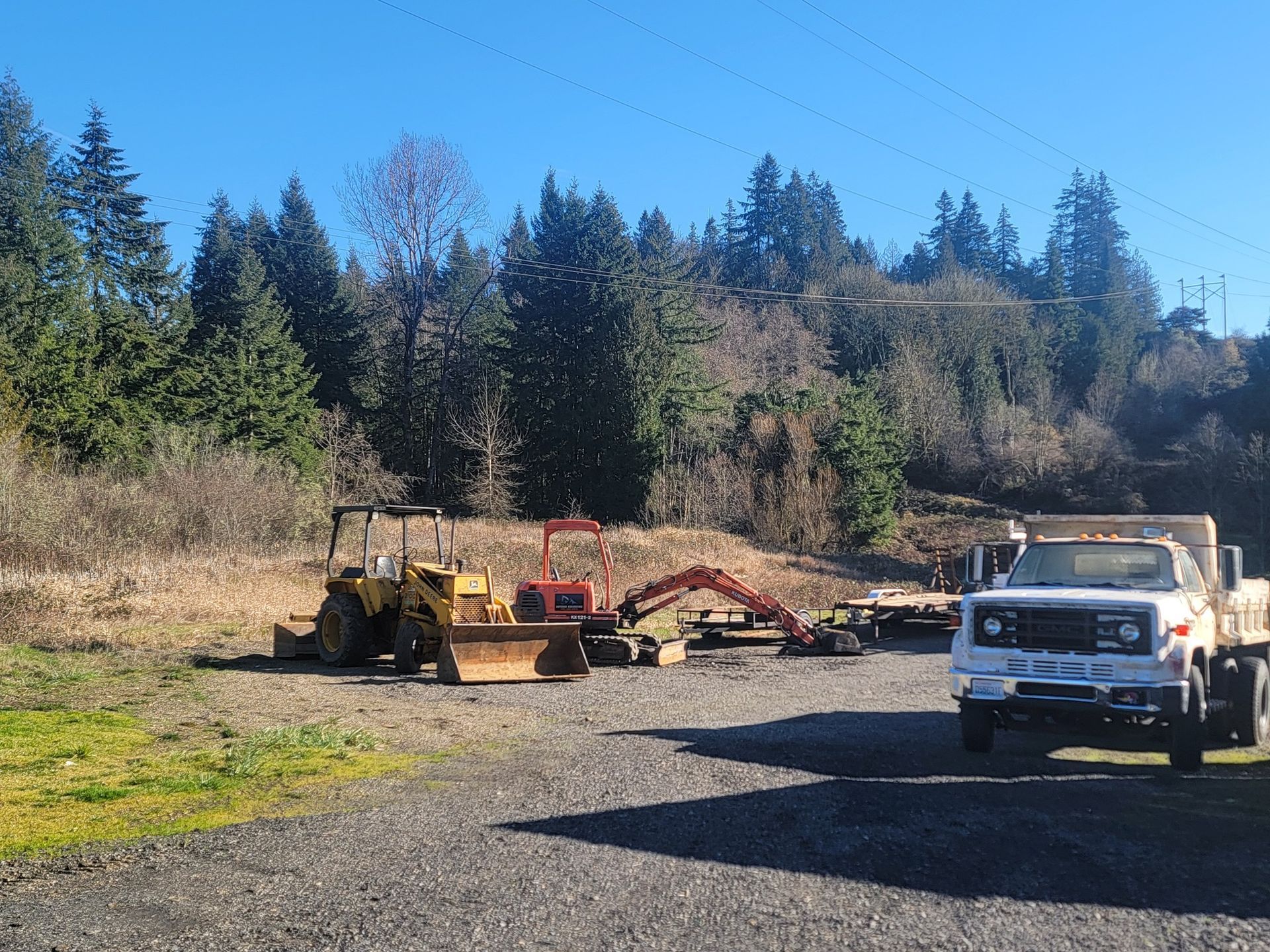 A white truck is parked in a gravel lot next to a bulldozer and an excavator.